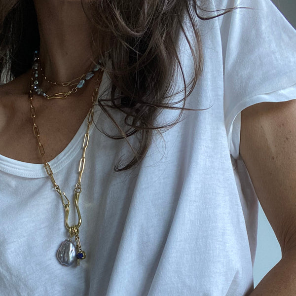 Woman with brown hair wearing a white t shirt and gold colored and pearl jewelry with a gold colored charm necklace